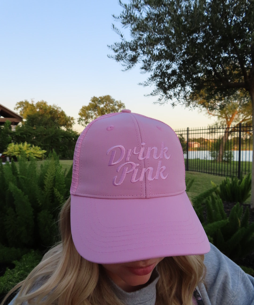 Woman wearing The Drink Pink Trucker Hat by Cold Beer Clothing Co., featuring pink embroidered Drink Pink lettering on the front in support of breast cancer awareness.