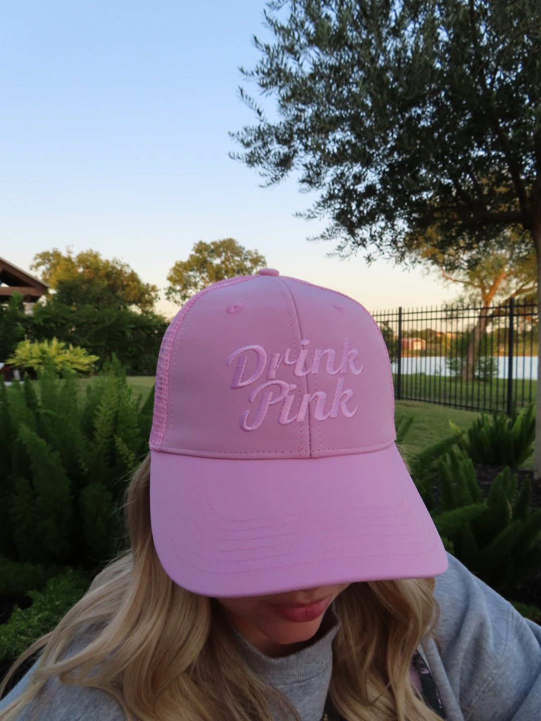 Woman wearing The Drink Pink Trucker Hat by Cold Beer Clothing Co., featuring pink embroidered Drink Pink lettering on the front in support of breast cancer awareness.