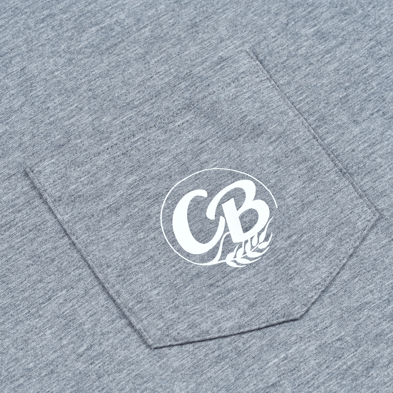 Close-up of the chest pocket on The Fully Stocked Long Sleeve Tee by Cold Beer Clothing Co., featuring heather gray fabric and the white CBC logo.