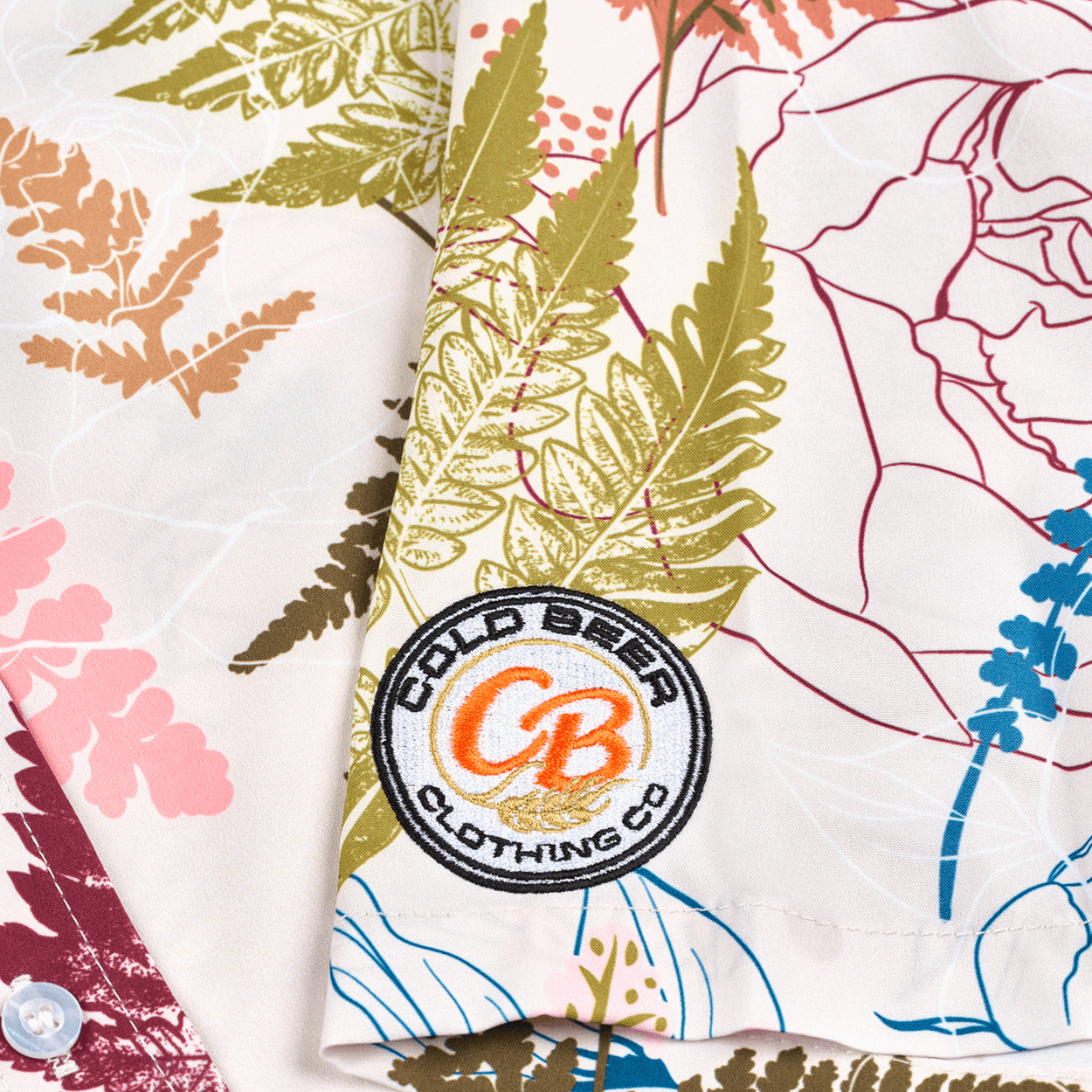 Close-up of the embroidered Cold Beer Clothing Co. logo patch on the left sleeve of the Vintage Big Leaf Button Down, featuring a colorful tropical leaf print.